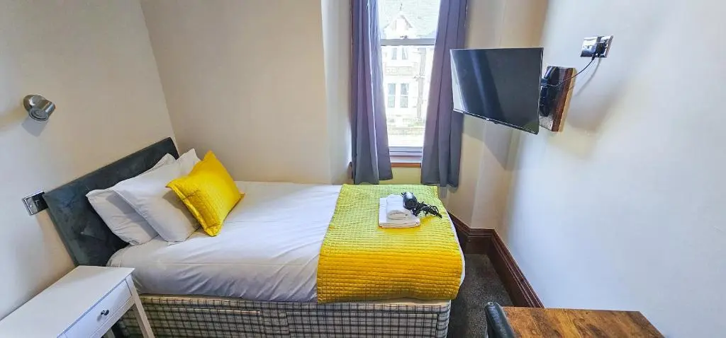 a small room with a bed with yellow pillows and a television at mySTAYINN Melrose Villa in Inverness