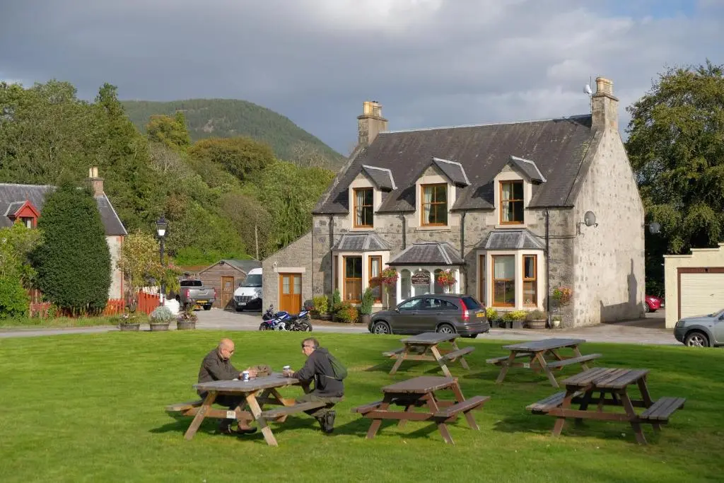 two men sitting at picnic tables in front of a building at Morlea Bed & Breakfast in Drumnadrochit