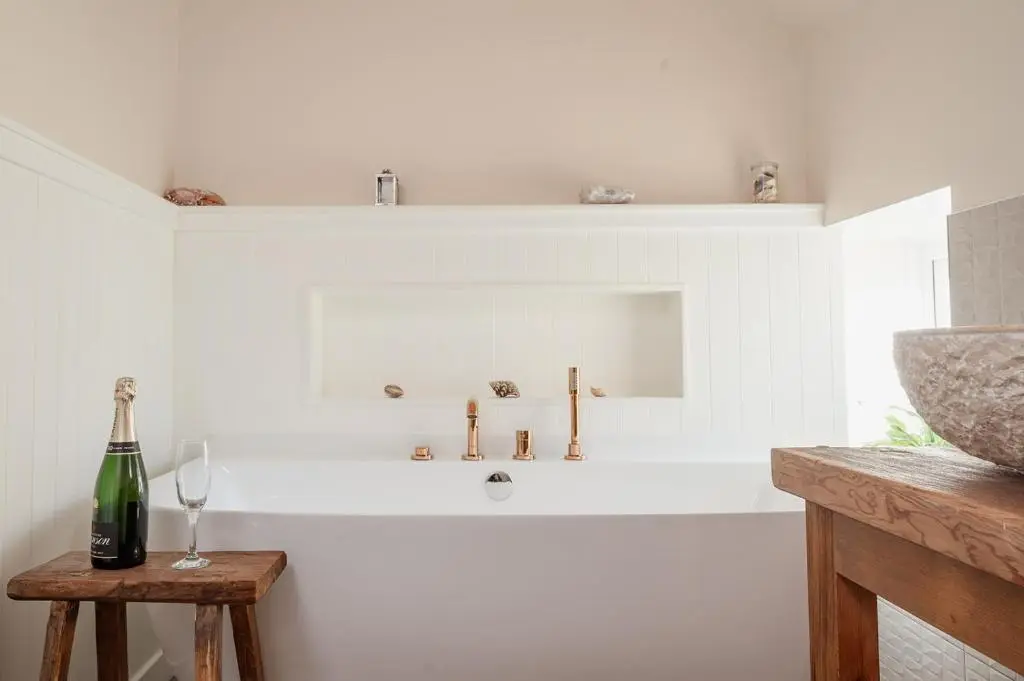 a white bath tub with a sink and a bottle of wine at Ina's Cottage - Seasgair Lodges in Portmahomack