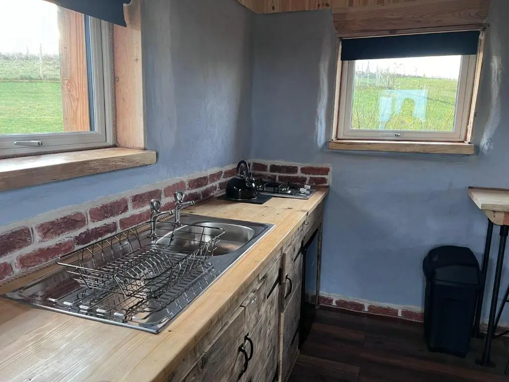 a kitchen with a sink and a stove and two windows at Primrose Straw Bale Cabin