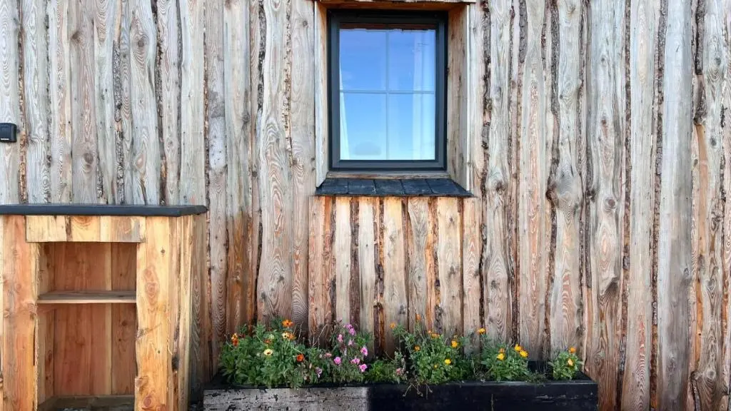 a window on a wooden building with flowers at Honeysuckle Straw Bale Cabin