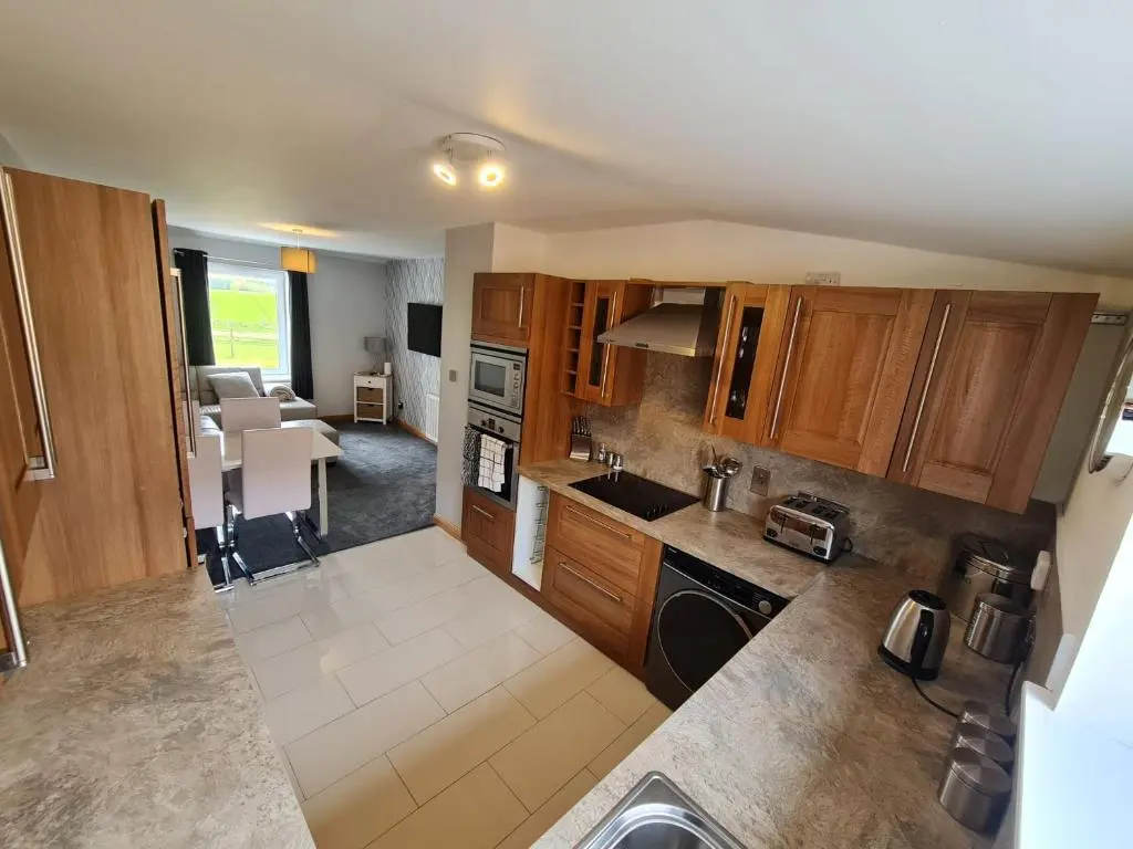 a kitchen with wooden cabinets and a living room at Bruxie Holiday Cottages - River Cottage in Maud