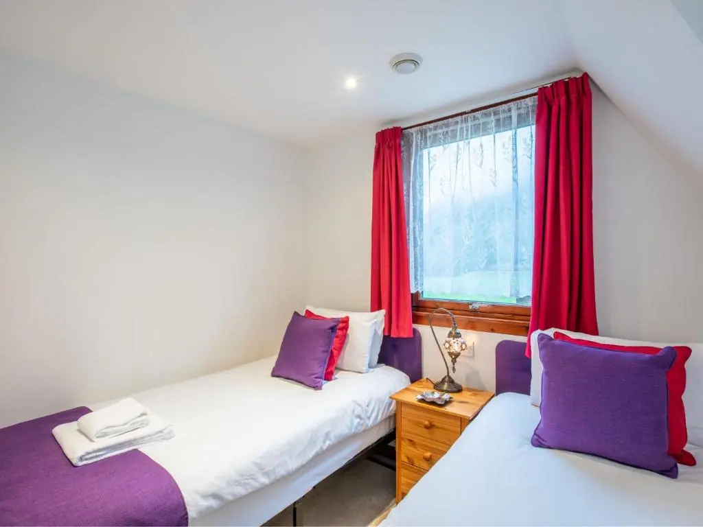 a bedroom with two beds and a window with red curtains at Chalet Lothlorien Lodge 4 by Interhome in Spean Bridge
