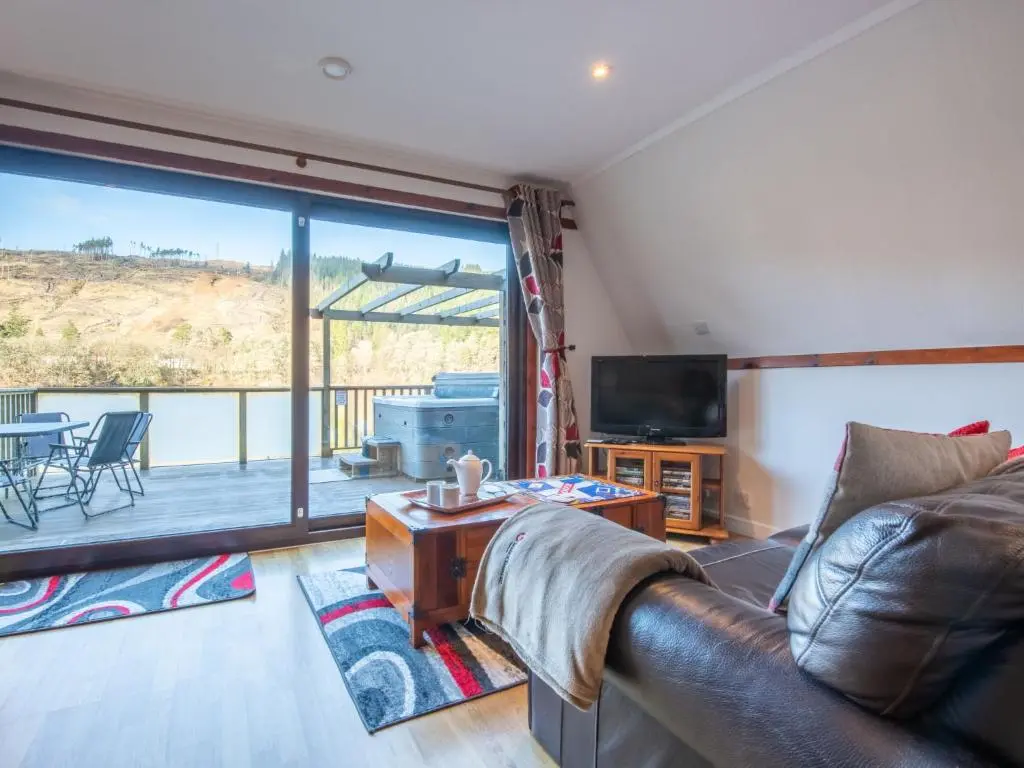 a living room with a leather couch and a television at Chalet Woodhaven by Interhome in Spean Bridge