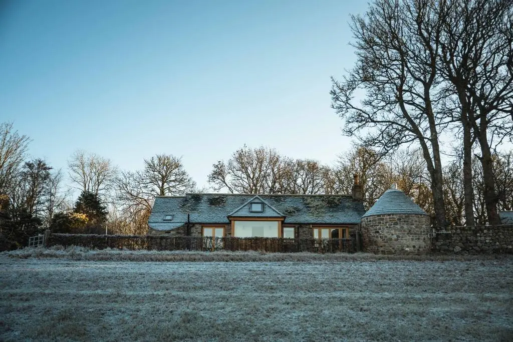 a house in a field with a stone wall at Kinkell Cottage in Dingwall