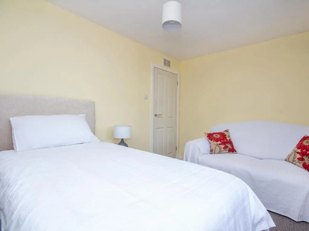 a bedroom with a white bed and a chair at Black Rock Cottage in Culbokie