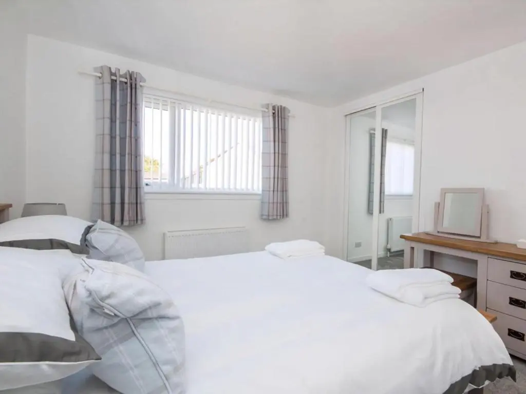 a white bedroom with two beds and a television at Raasay in Dornoch