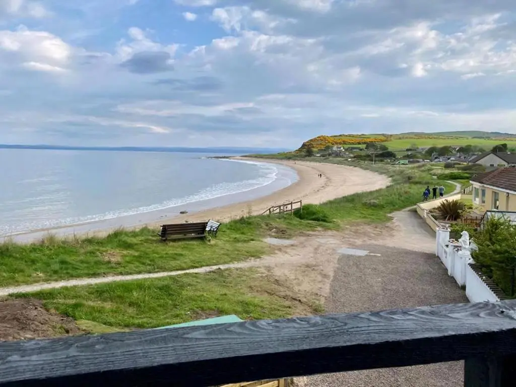 a view of a beach with a bench and the ocean at On The Beach-Uk7465 in Balintore