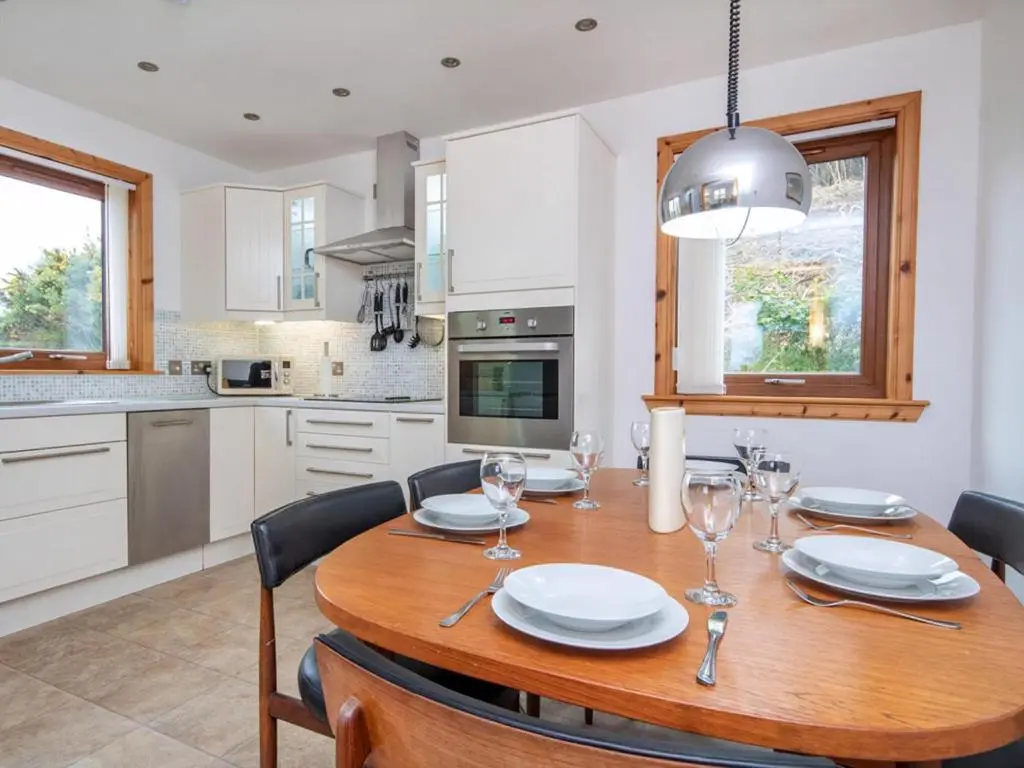 a kitchen with a wooden table with plates and wine glasses at Lower Whinhill in Evelix