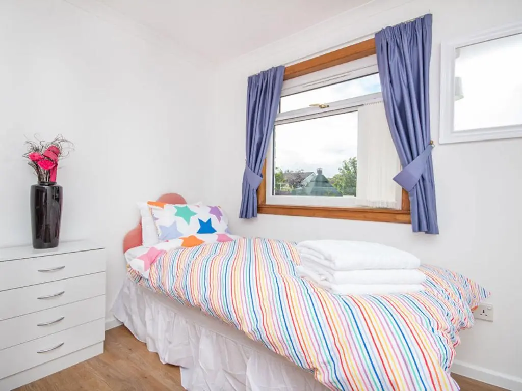 a bedroom with a bed with blue curtains and a window at Caledon in Aviemore