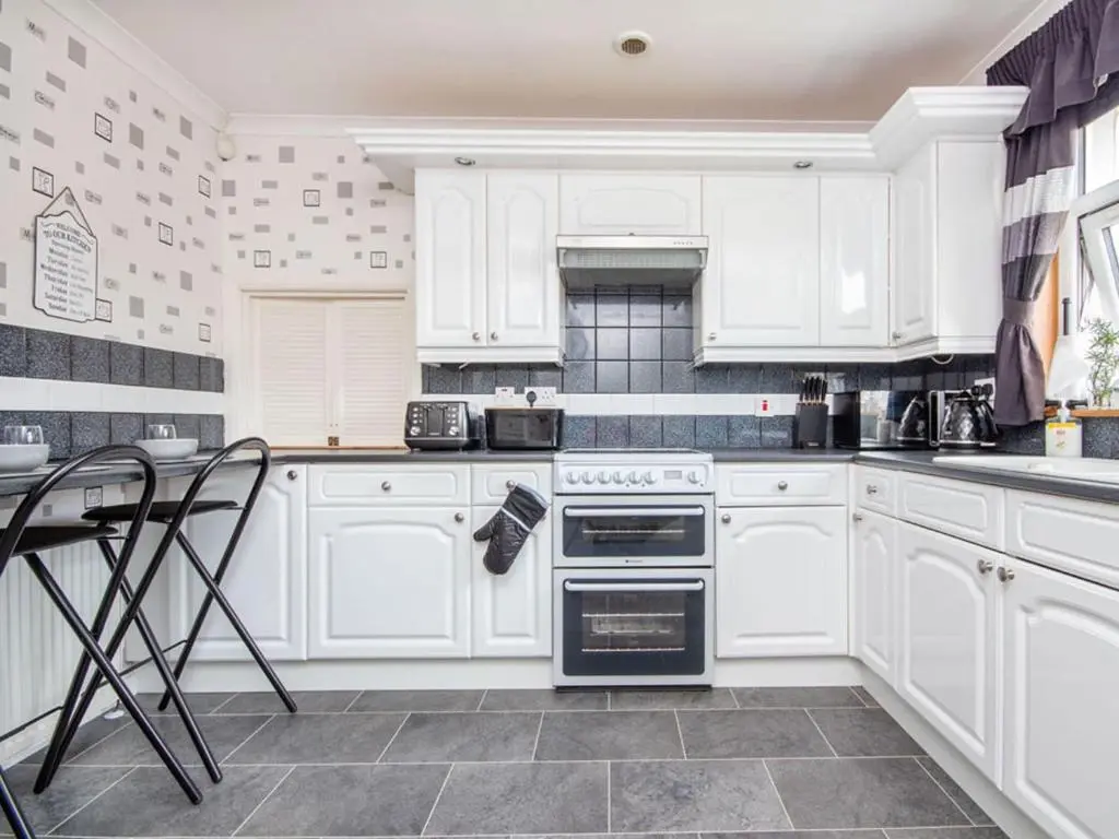 a white kitchen with white cabinets and a stove at Caledon in Aviemore