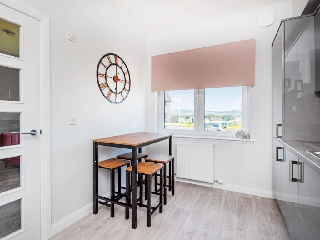 a kitchen with a table and stools and a clock on the wall at Kessock View Apartment in Inshes
