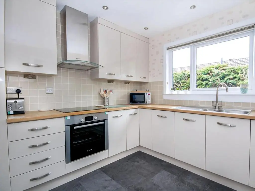 a white kitchen with white cabinets and a window at 58 Moray Park in Culloden