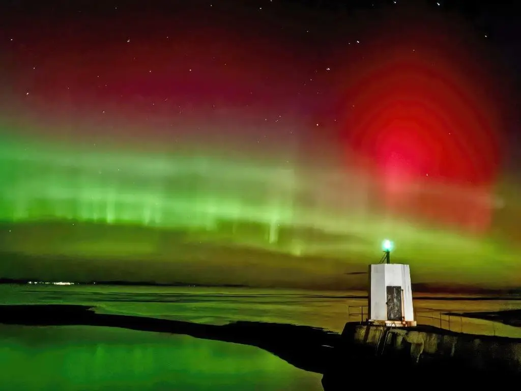 an aurora over the water with a lighthouse at Reay House in Nairn