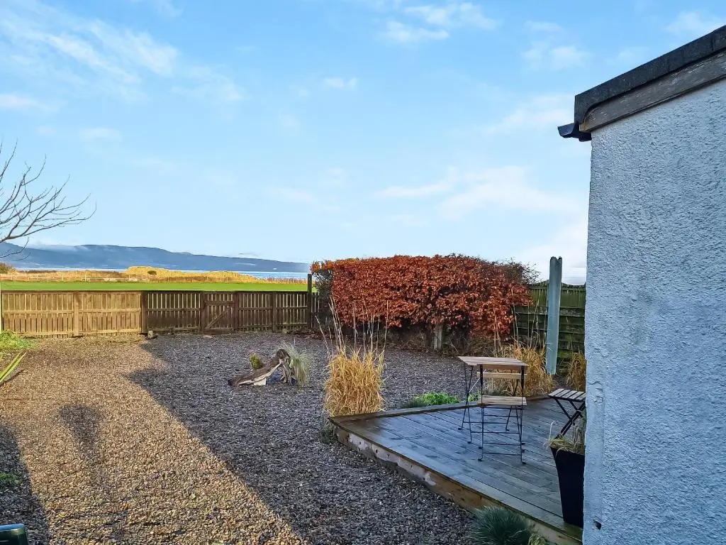 a backyard with a wooden deck and a fence at Sunnyside Cottage in Embo