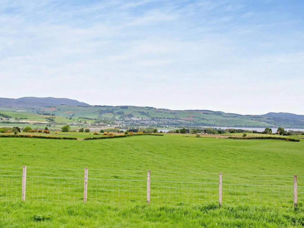 a fence in a green field with mountains in the background at 2 Bed in Conon Bridge CA387 in Cononbridge