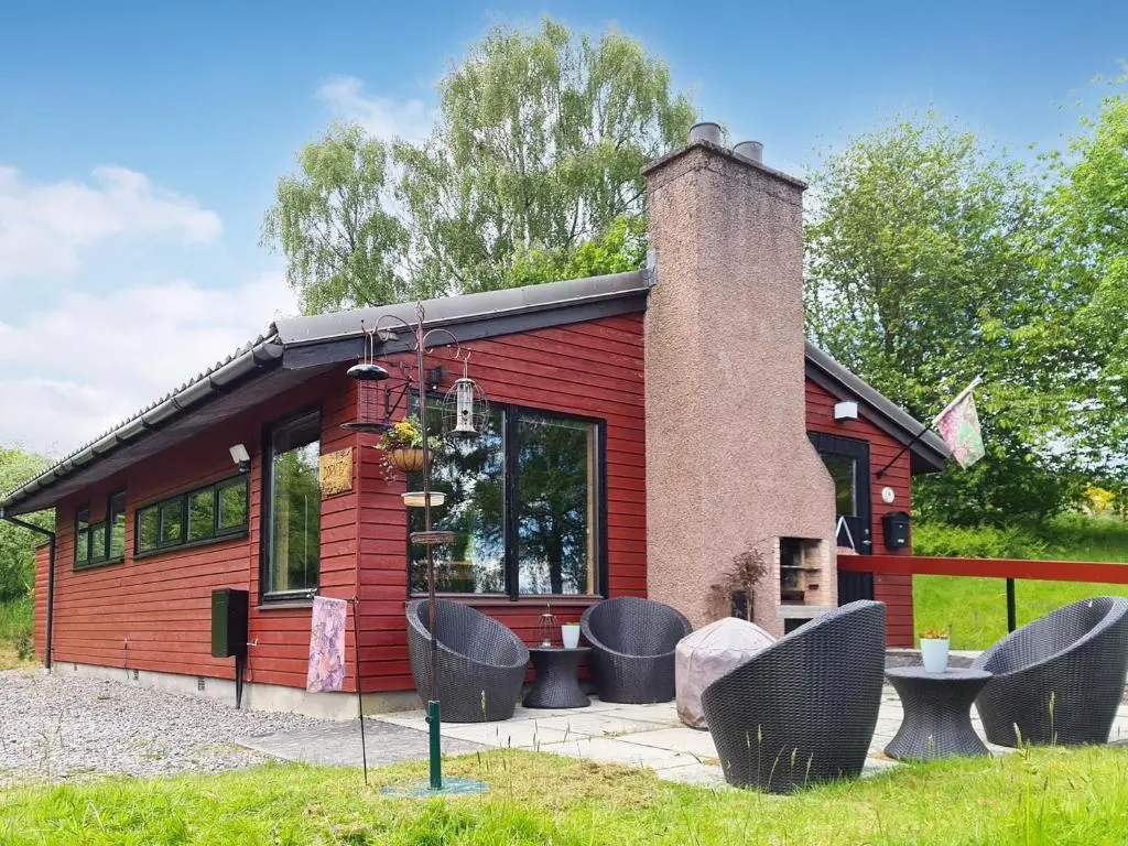 a red cabin with a chimney and some chairs at Dornie Lodge in Beauly