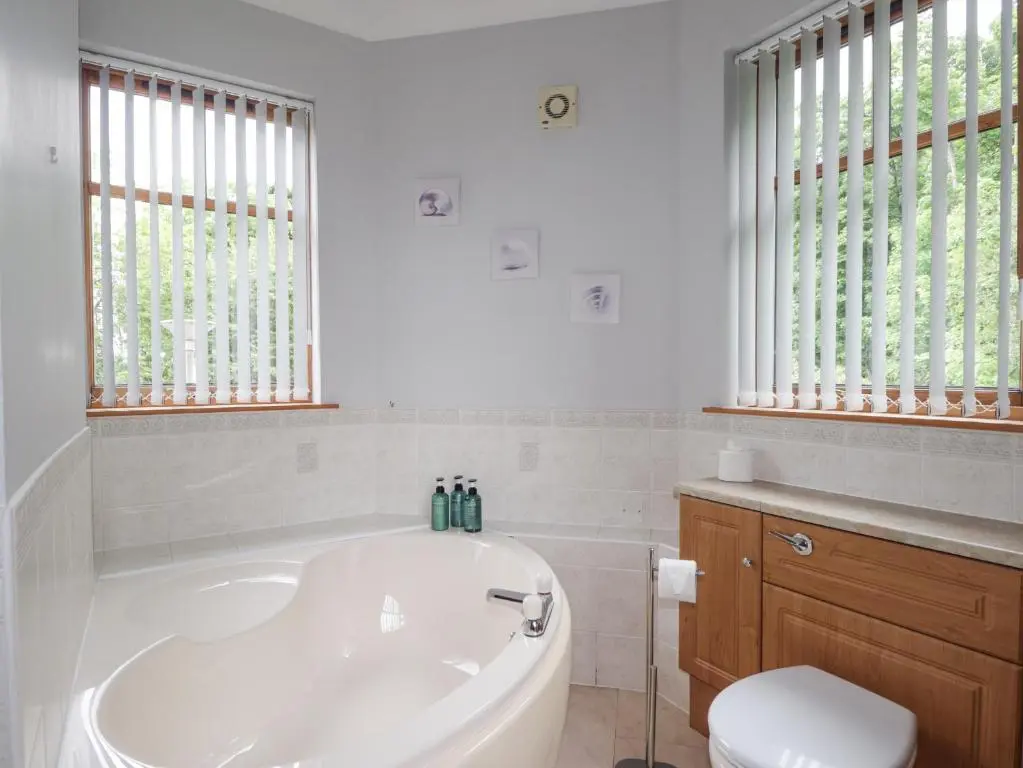 a bathroom with a tub and a toilet and windows at Rossie Lodge in Inverness