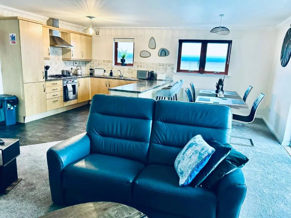 a living room with a blue couch and a kitchen at Central Cosy Riverview Apartment 2 bed, 2 bath, Free Parking / WiFi in Inverness