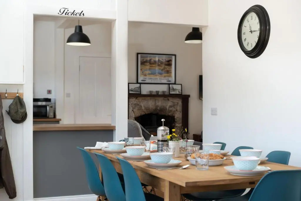 a dining room table with blue chairs and a clock at Nethy Station - Seasgair Lodges in Nethy Bridge