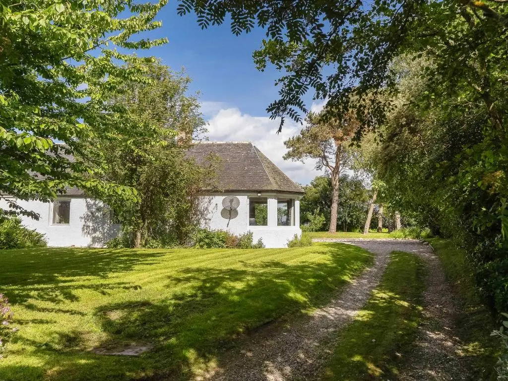 a white house on a grassy yard with a dirt road at East Tarrel Cottage in Portmahomack