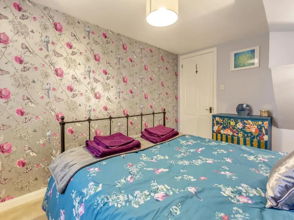 a bedroom with a bed with purple sheets and floral wallpaper at East Tarrel Cottage in Portmahomack