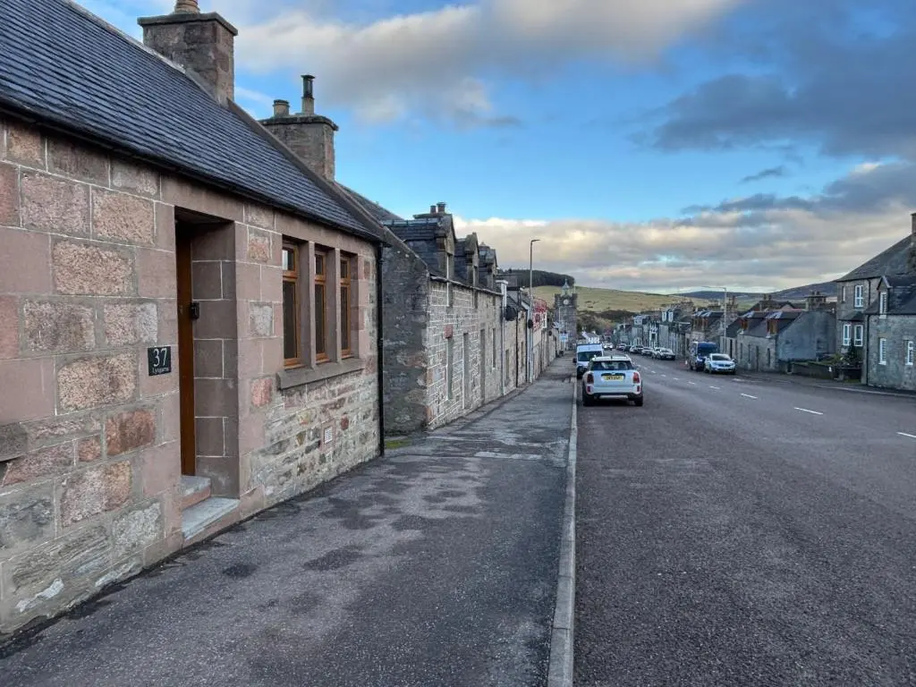 an old brick building with a car parked on a street at Lyngarrie in Dufftown