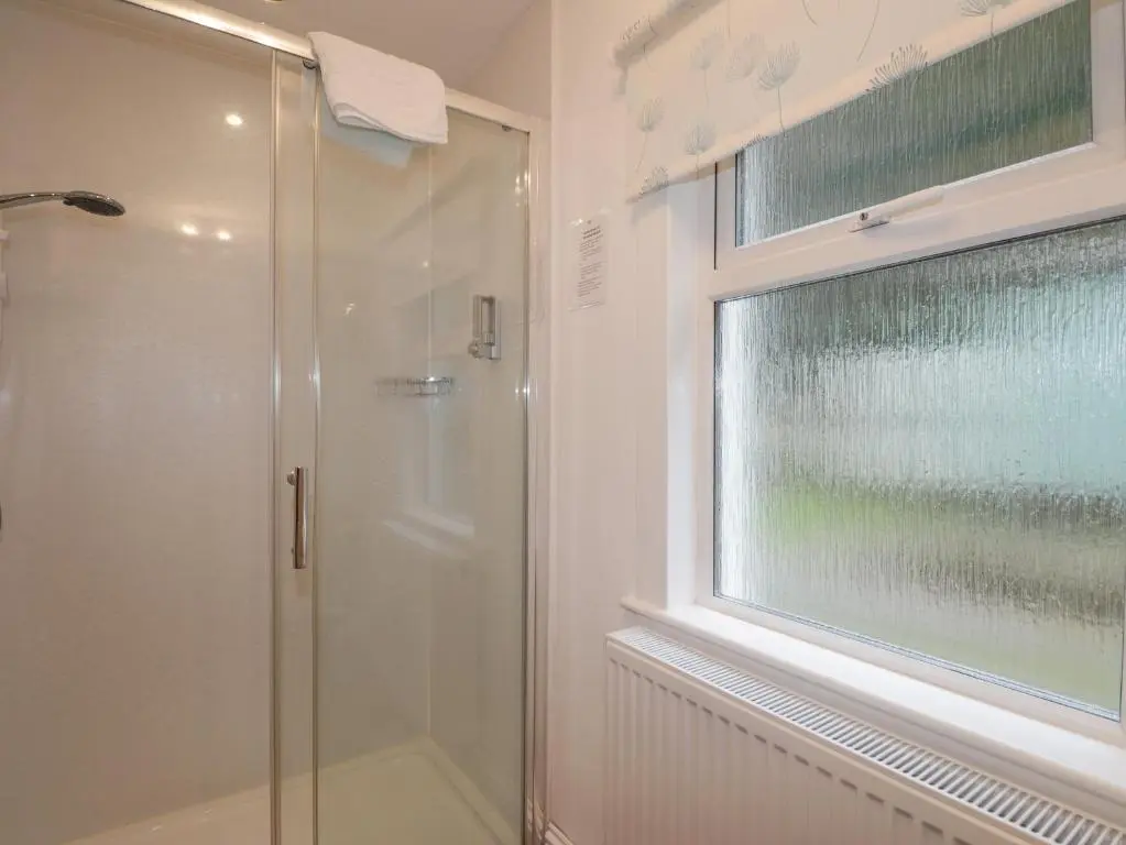 a shower with a glass door next to a window at Arden House in Kingussie