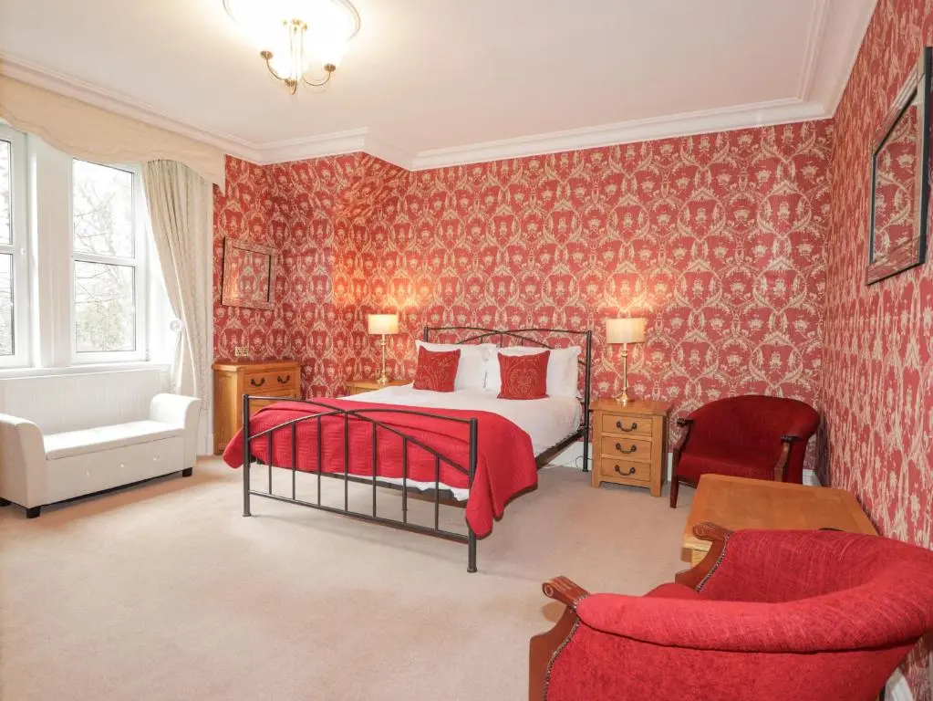 a bedroom with red wallpaper and a bed and two chairs at Arden House in Kingussie