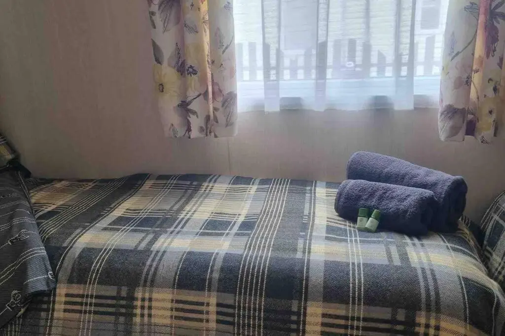 a bedroom with a bed with a blanket and a window at Coorie Nook, Chalet 103 in Aviemore
