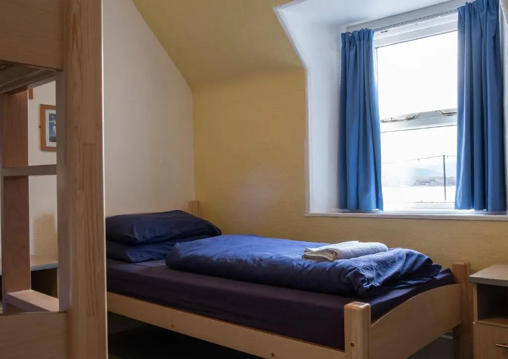 a bedroom with a bed with blue sheets and a window at Ullapool Youth Hostel in Ullapool