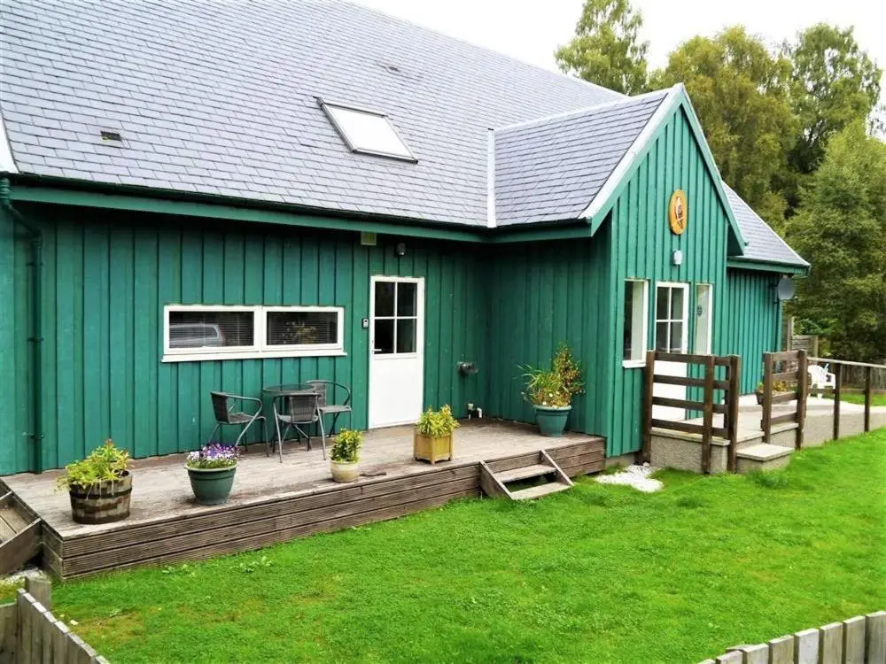 a green house with a wooden deck in the yard at Osprey Cottage in Aviemore