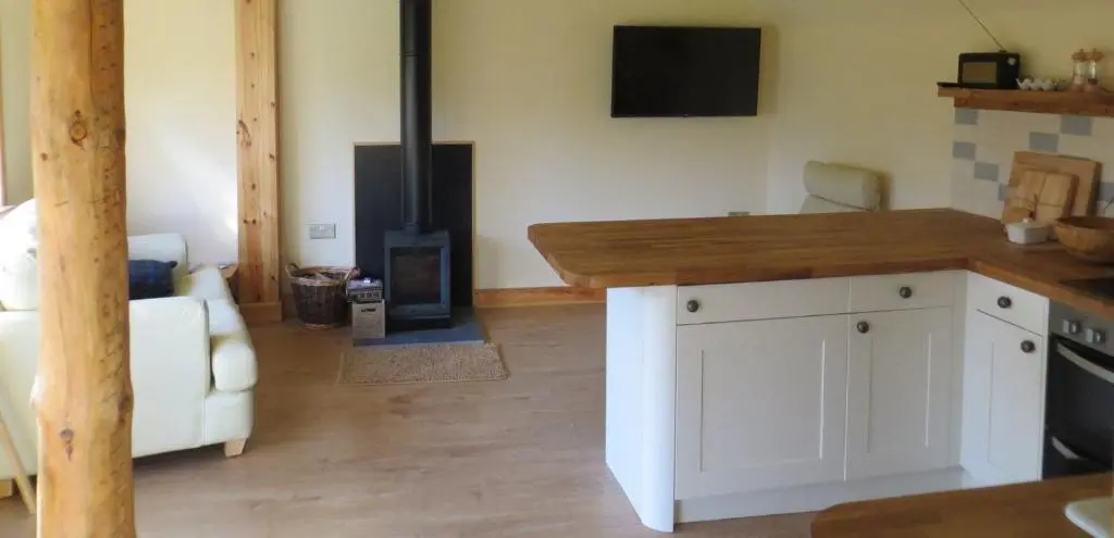 a living room with a stove and a white kitchen at Sycamore Cottage in Boat of Garten