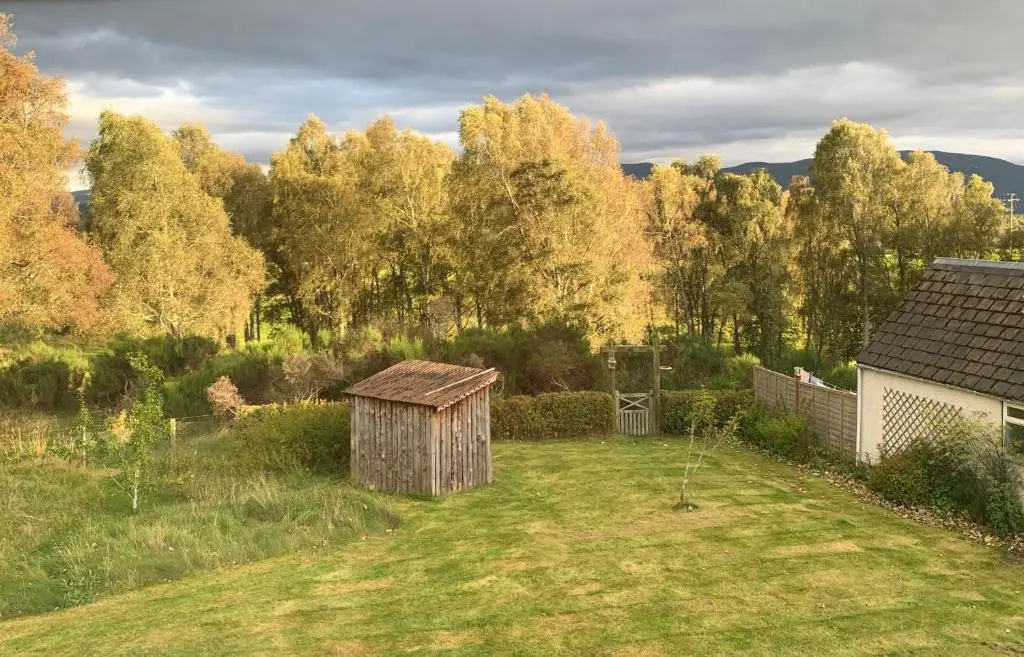 a garden with a wooden shed in the grass at Locheil Apartment in Boat of Garten