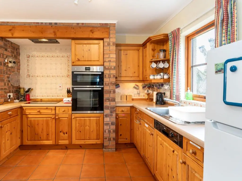 a kitchen with wooden cabinets and a brick wall at Holiday Home Lower Curr by Interhome in Skye of Curr