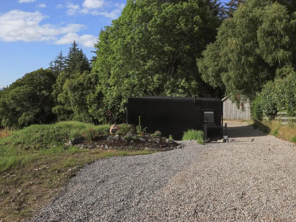 a gravel road next to a black building on a hill at Core-na-bye in Inverness