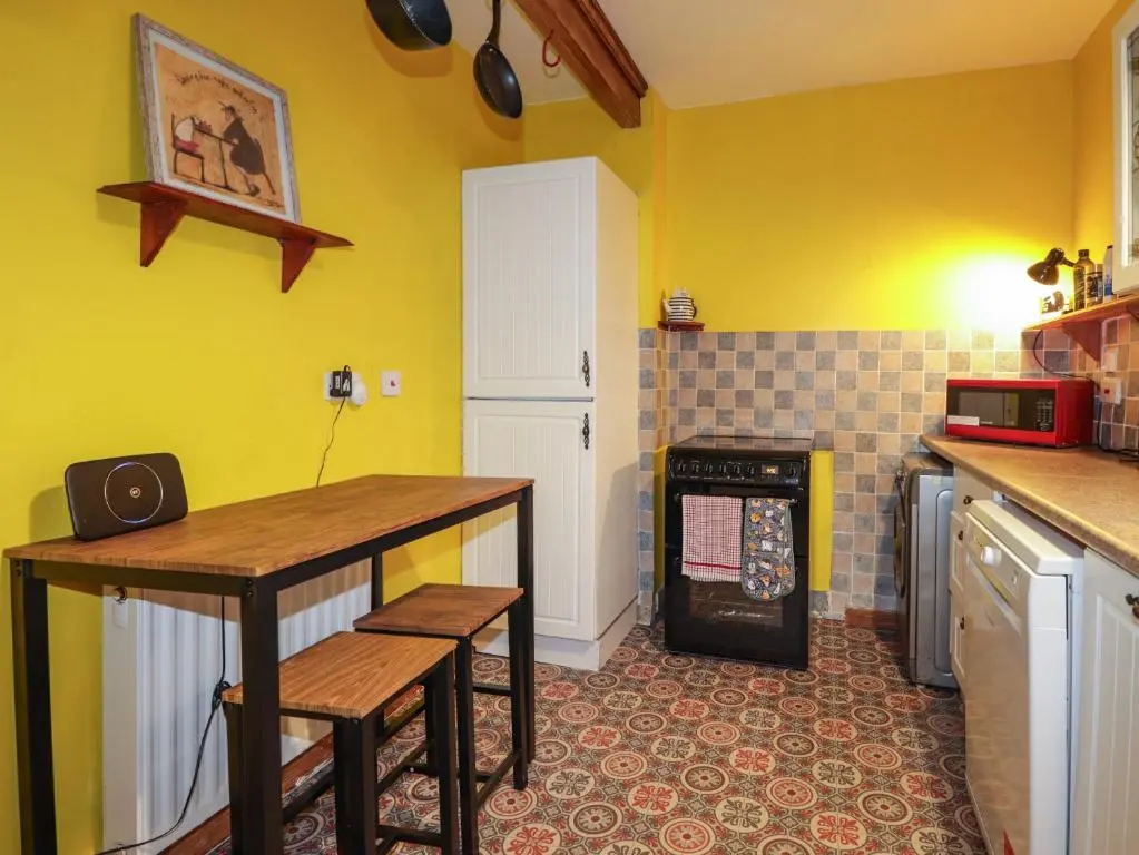 a kitchen with yellow walls and a table and a stove at Rowan Tree House in Brora
