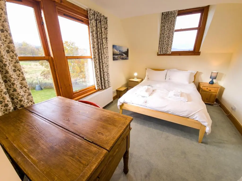 a bedroom with a bed and a table and windows at Carriden in Insh