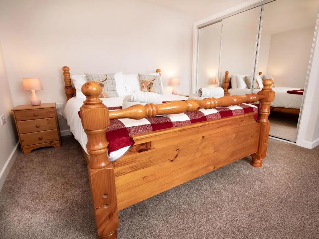 a large wooden bed in a bedroom with a mirror at Cranberry Cottage in Wick