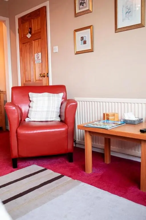 a red chair sitting in a living room with a table at Fonthill Bed and Breakfast Nairn in Nairn