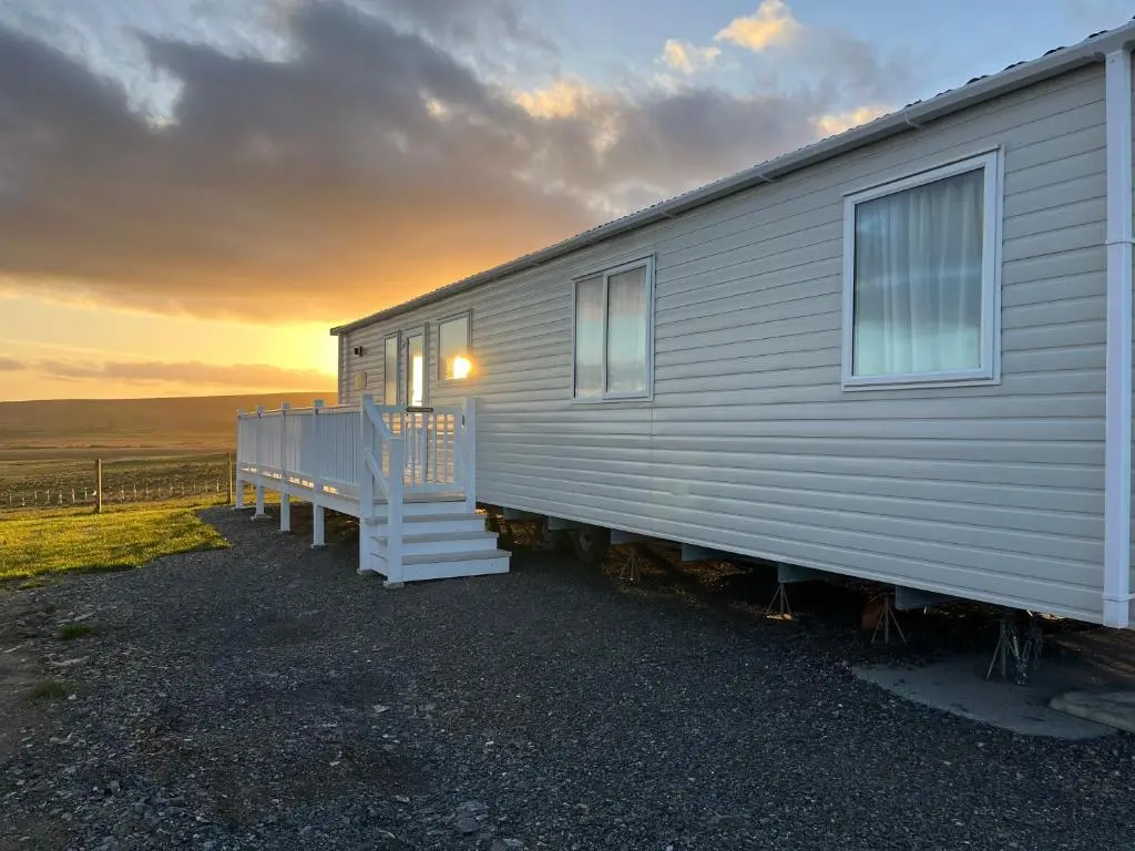 a house with a porch and a sunset in the background at Robyn\u2019s Nest in Lybster