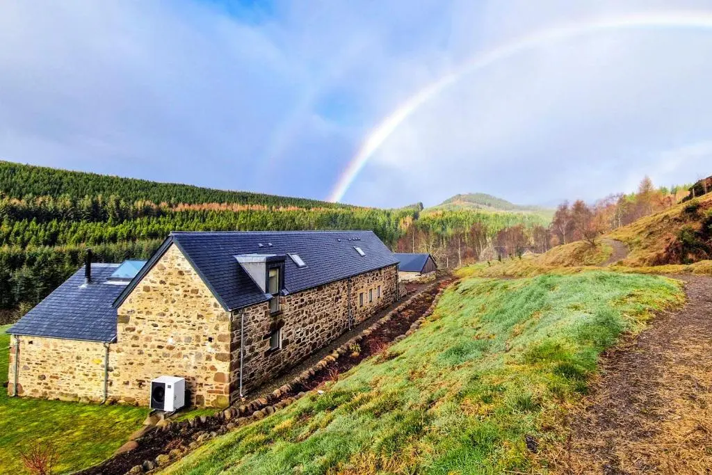 a rainbow over a stone house in a field at Greenhill Cottage in Evanton