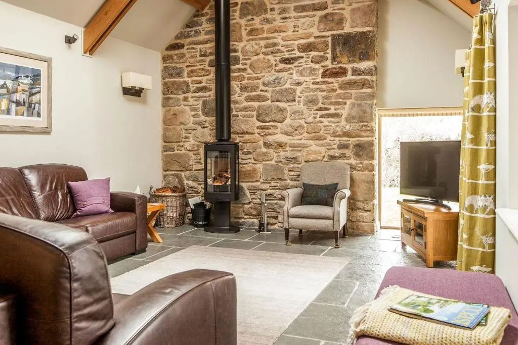 a living room with leather furniture and a stone wall at Greenhill Cottage in Evanton