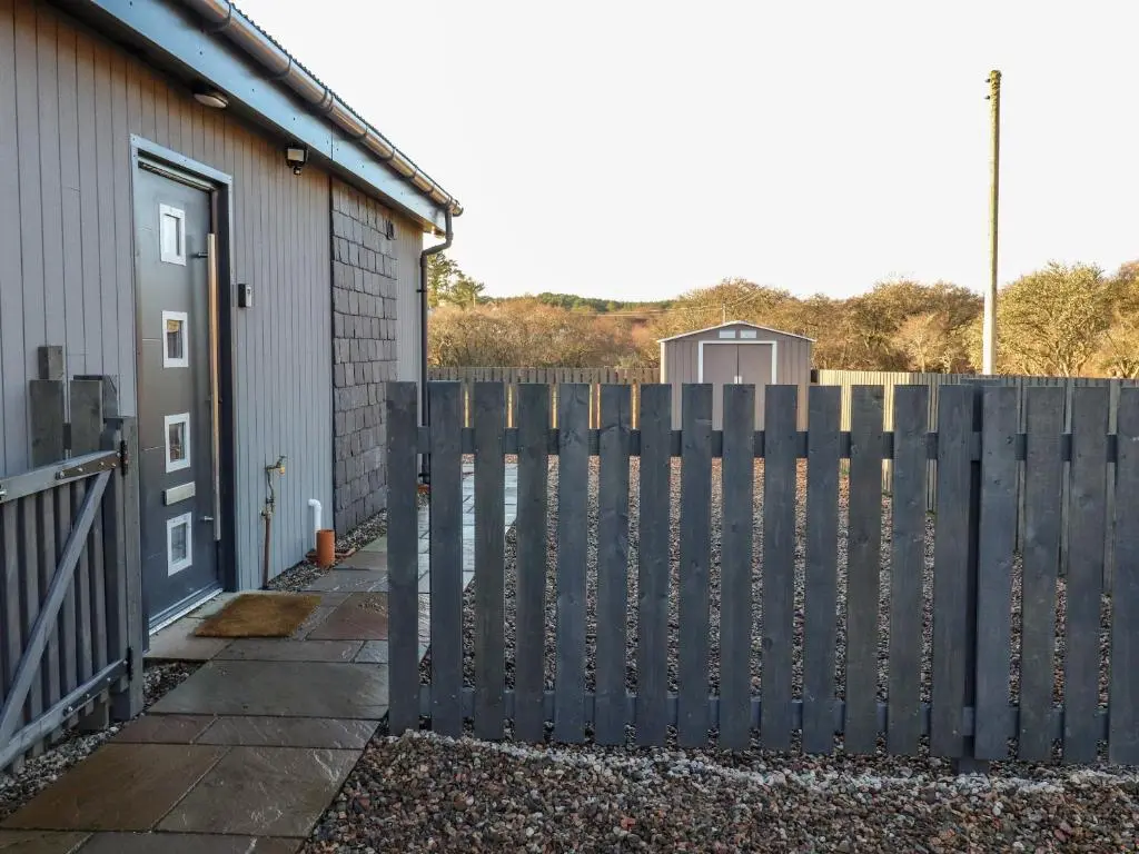 a fence in front of a building with a door at Pine Marten in Dornoch