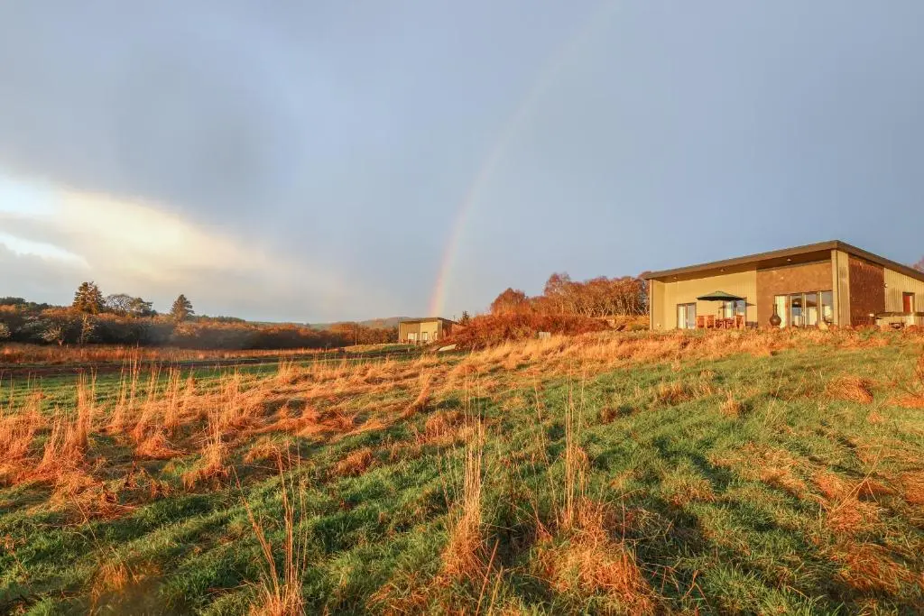 a house in a field with a rainbow in the background at Red Squirrel in Dornoch