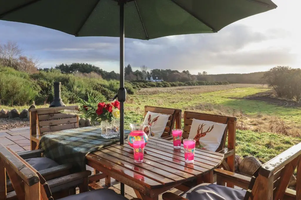 a wooden table with a green umbrella on a patio at Red Squirrel in Dornoch