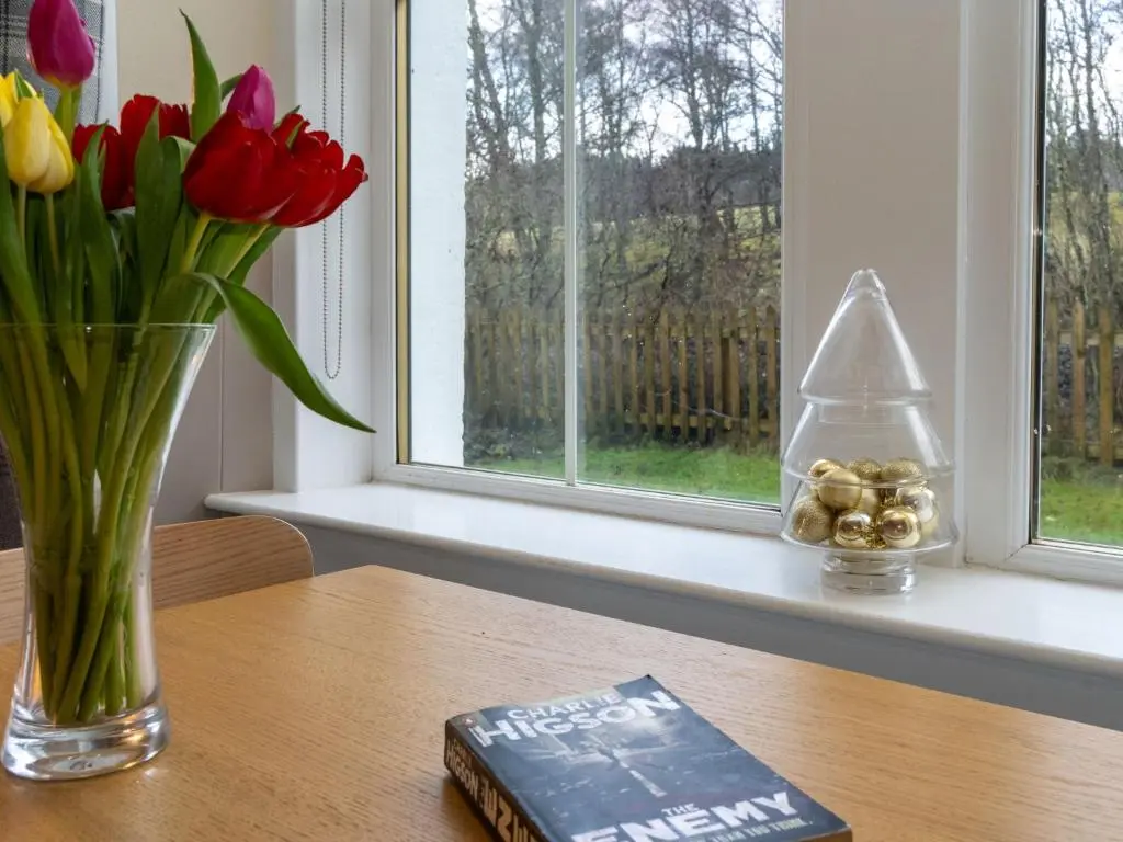 a vase of flowers and a book on a table at Holiday Home Railway House by Interhome in Aviemore