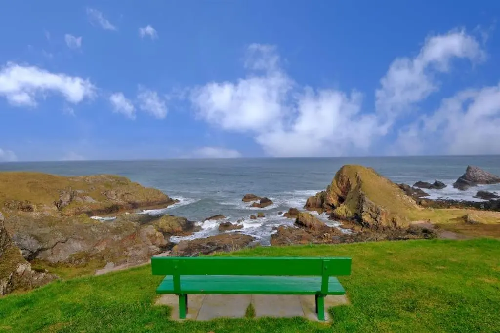 a green bench sitting on a hill overlooking the ocean at Cliff Top Cottage with Sea Views in Portknockie
