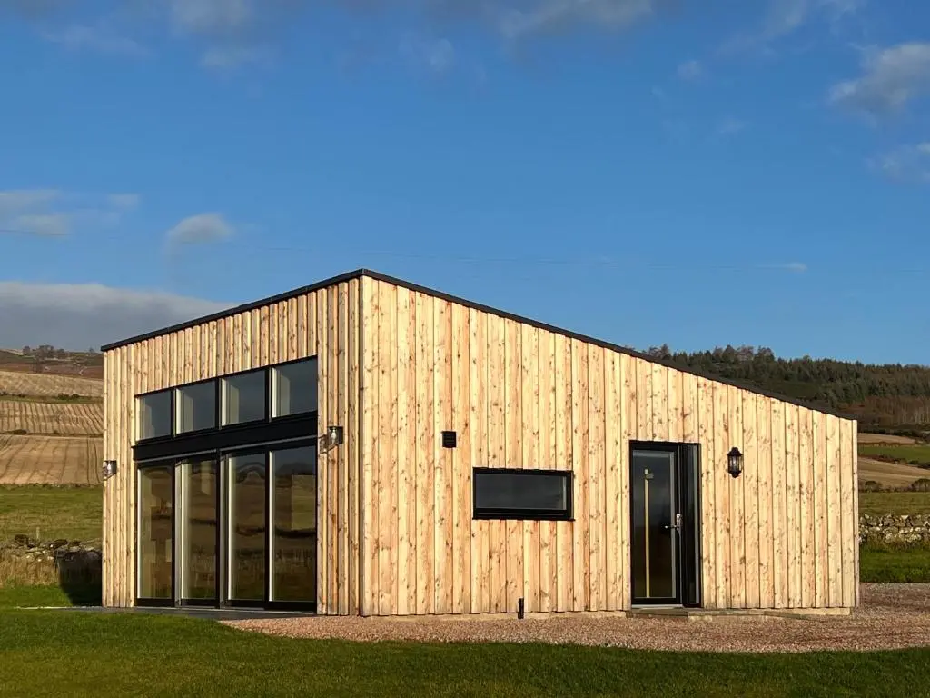 a wooden building with a large door in a field at Tillyfruskie Farm Holiday Cabin, Finzean in Banchory