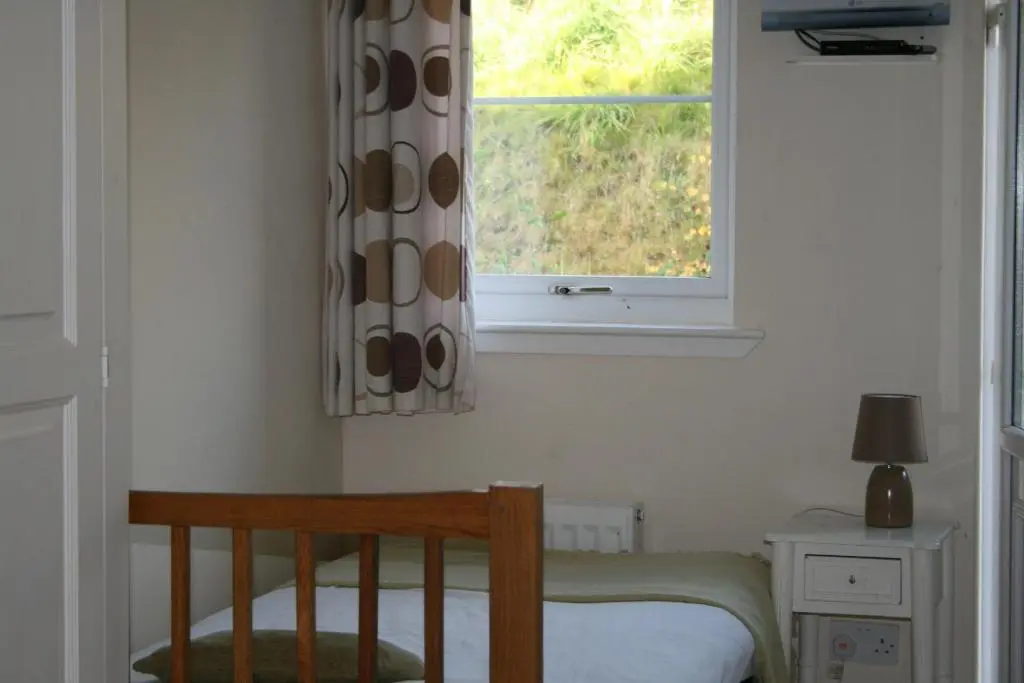 a bedroom with a bed and a window and a chair at BCC Loch Ness Hostel in Bearnock